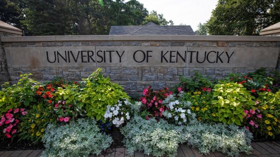 University of Kentucky etched into stone wall bordering a flowerbed at the entrance to campus.